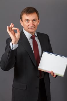 Confident and friendly elegant handsome mature businessman standing in front of a gray background holding a notebook