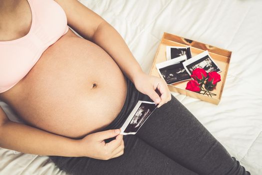 Pregnant woman feeling happy at home while taking care of her child. The young expecting mother holding baby in pregnant belly. Maternity prenatal care and woman pregnancy concept.