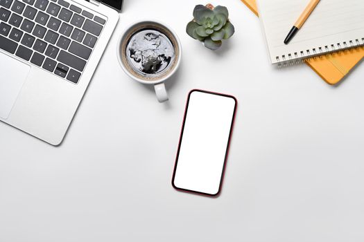 Mockup mobile phone with lank screen, laptop, coffee cup and notepad on white office desk.