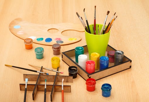Wooden palette with colorful paints and cup with paintbrushes on the table