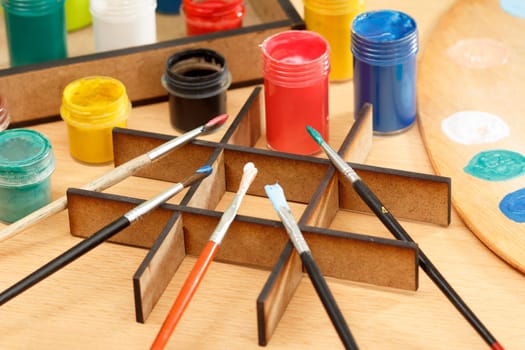 Wooden palette and box with paints and paintbrushes on wooden desk