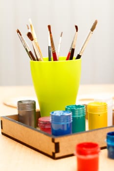 Paintbrushes in a cup and paints in box on wooden table