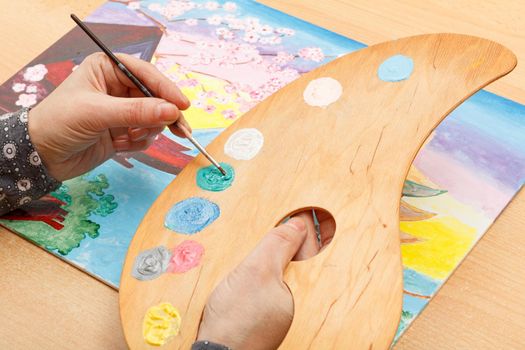 Artist painting Japanese landscape indoors on the wooden desk with palette