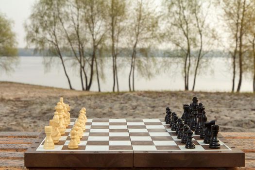 Chess board with chess pieces on river embankment. Chess game with wooden chess pieces