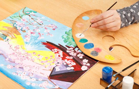 Woman's hand painting Japanese landscape indoors on the wooden table with brush and palette Artist in her workshop
