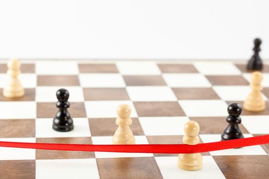 White pawn's figure crossing the red finish ribbon. Chess leadership and success concept