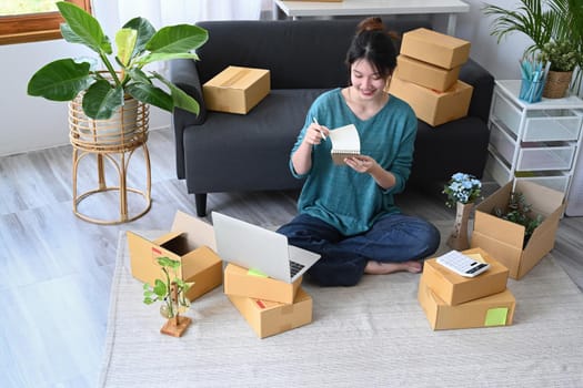 Young start up small business entrepreneur sitting in her home office and preparing parcel boxes for delivery.