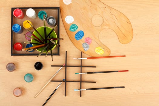 Wooden palette and box with paints and paintbrushes on wooden desk. Top view.