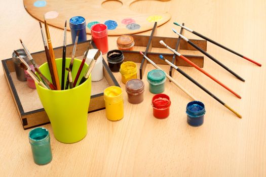 Drawing set Wooden palette with laying on paints and cup with paintbrushes on the table