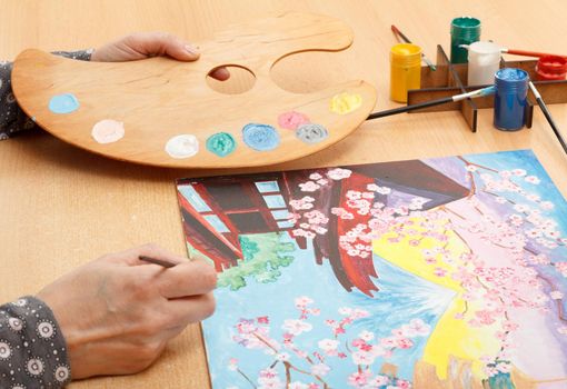 Woman's hand painting Japanese landscape indoors on the wooden desk with palette
