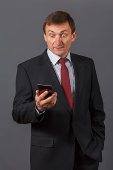 Confident elegant handsome mature businessman standing in front of a gray background in a studio wearing a nice suit is speaking on the sell phone