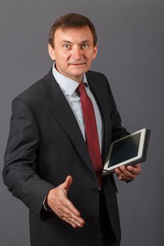 Confident and friendly elegant handsome mature businessman standing in front of a gray background in a studio giving a hand for greetings