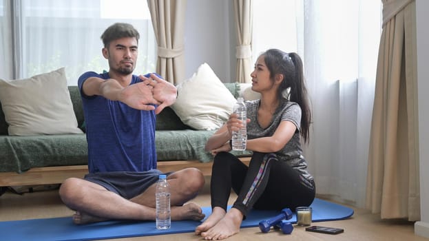 Shot of young couple in sportswear resting and drinking water after workout at home.