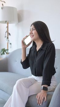 Portrait young woman sitting on couch and having conversation with mobile phone.