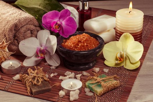 Spa and wellness setting with orchid flowers, bowl with sea salt, seashell, bottle with aromatic oil, soap, candles and towels on bamboo napkin