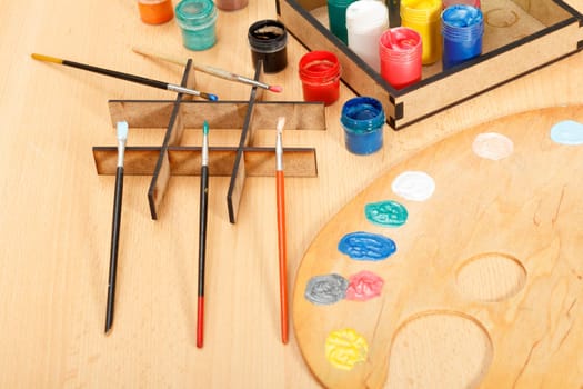 Wooden palette and box with paints and paintbrushes on wooden desk