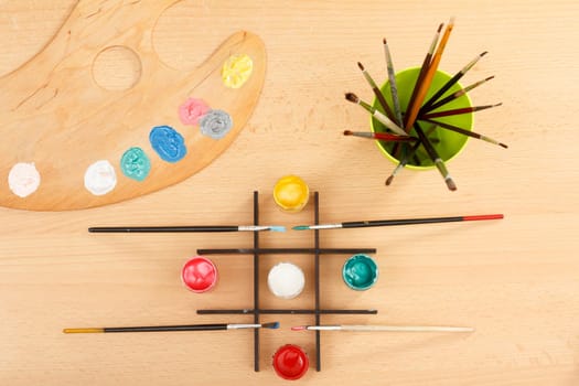 Palette with colorful paints and paintbrushes in a cup on wooden desk Drawing set