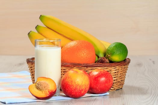 Glass of delicious yogurt with mint and fresh strawberries, banana, lime, nectarine, orange in a wicker basket on a wooden table