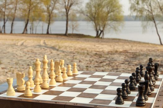 Chess board with chess pieces on river embankment. Outdoors chess game with wooden chess pieces
