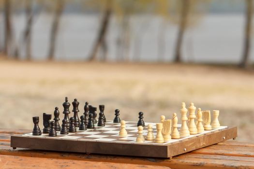 Chess board with chess pieces on wooden bench. Outdoors chess game