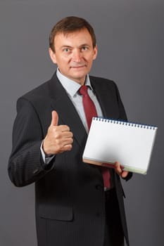 Confident and friendly elegant handsome mature businessman standing in front of a grey background holding a notebook