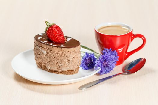 Chocolate cake with strawberry on the white plate, cornflowers and a cup of coffee on a wooden table