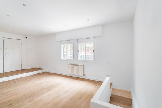 Empty white room with windows and hardwood floor after renovation. New apartment for rent or sale
