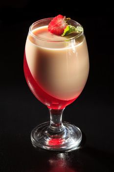 Cherry and milk jelly in the glass topped mint leaves and strawberry piece on the black background