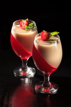 Cherry and milk jelly in the glasses topped mint leaves and strawberry pieces on the black background