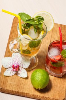 Cold refreshing summer lemonade mojito with lemon slices and mint in a tall glass and strawberry lemonade with mint in a short one on wooden cutting board. Top view.