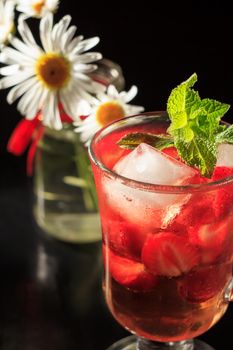 Carbonated lemonade with strawberry slices and mint with flowers of chamomile on the black background. Cold beverage for hot summer day