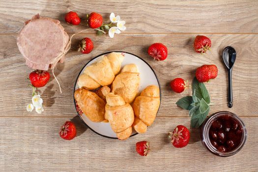 Traditional homemade strawberry jam in jars and plate with croissants, decorated with fresh strawberries Top view