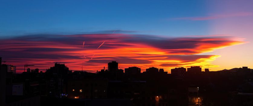 Amazing sunset with orange, pink and red stratus clouds over the city with traces from the plane in the sky. Background for forecast and meteorology concept. Barcelona, Spain.