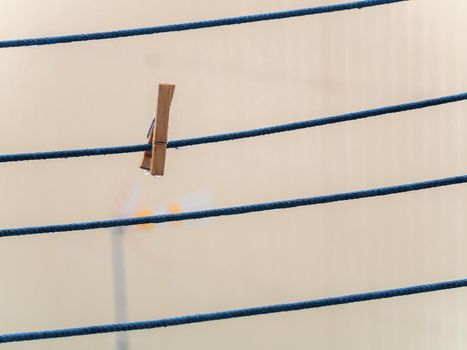 One wooden clothespin on a blue rope with hanging waterdrops after the rain with copy space. Wet clothesline with clothes clip.