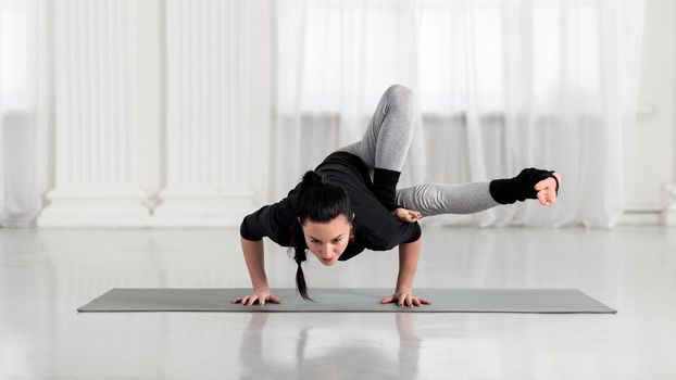 Young asian attractive woman practicing yoga, standing in Dragonfly exercise, Maksikanagasana, Parivrtta Eka Pada Danda Koundiniasana pose, working out, full length, white hall.