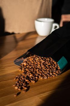 Coffee beans spilled out of the black plastic bag on the wooden background