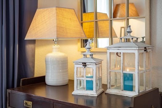 Vintage wooden lanterns, candle holders with blue burning candles inside, placed on dark table with lamp in a cozy room.