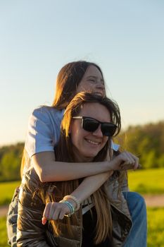 Playful mother giving daughter piggy back ride at green field. Both laughing and look happy. Spring in forest background. Closeup.