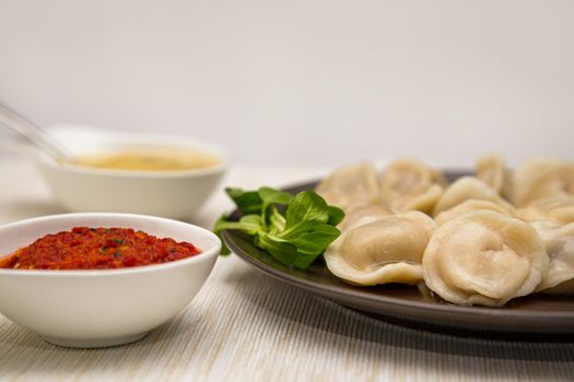 Russian food pelmeni meat dumplings with mustard and tomato sauce on a brown plate. Placed on a table with placemat. Close-up