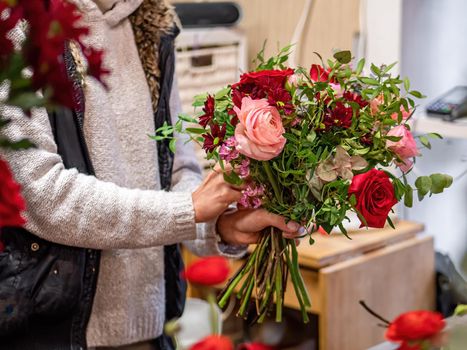 Florist makes beautiful bouquet of mixed roses and other flowers in a shop. Fresh cut flowers. Gift for Valentines day.