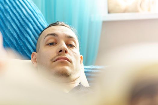 Man thoughtfully reading book comfortably lying on sofa. Selective focus