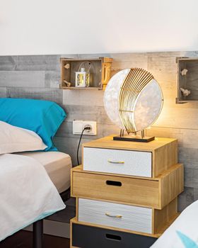 Comfort bed in cozy bedroom with night lamp on bedside at beach house interior. Vertical shot.