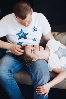 Young couple laying together on belly in bed at studio. Two people smiling and embracing, spending time together and having fun, both wearing in white t shirt. Concept of love and relationship.