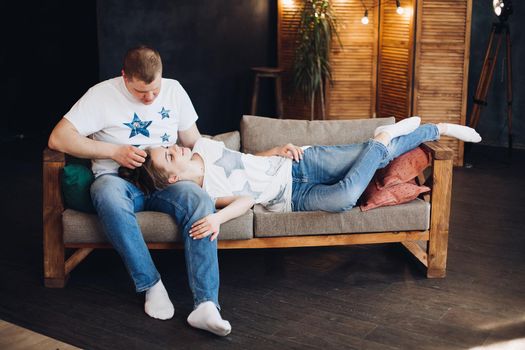 Young couple laying together on belly in bed at studio. Two people smiling and embracing, spending time together and having fun, both wearing in white t shirt. Concept of love and relationship.