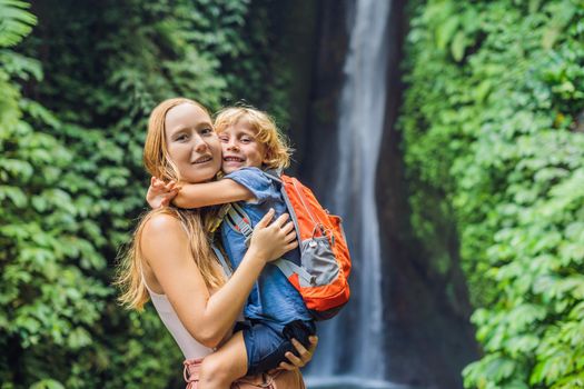 Mom and son travelers on the background of Leke Leke waterfall in Bali island Indonesia. Traveling with children concept.