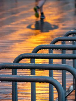 Bicycle parking lot on rainy evening with lights reflection and blurred legs of a running man. Rain drops hanging from a metallic stand.