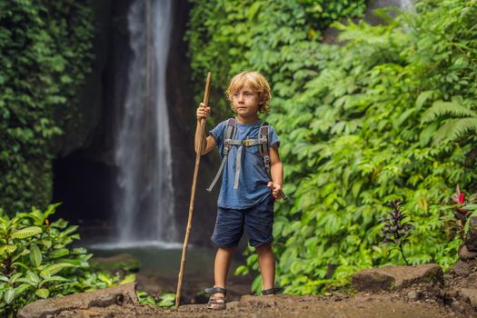 Boy with a trekking stick on the background of Leke Leke waterfall in Bali island Indonesia. Traveling with children concept.