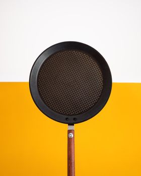 Flat metallic pancake pan with brown wooden handle on yellow and white background with copy space