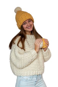Beautiful happy girl holding in her hands two yarn balls and wearing beige sweater and yellow cap, knitted thick thread. Handmade winter clothes. Isolated.