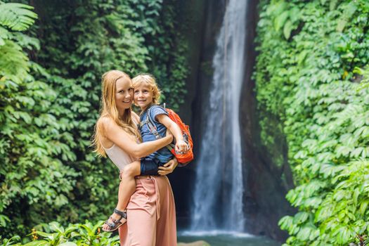 Mom and son travelers on the background of Leke Leke waterfall in Bali island Indonesia. Traveling with children concept.